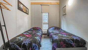 Een kleine kamer met twee bedden, een raam en een houten balk aan het plafond.