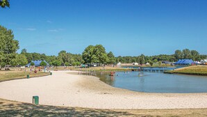 Uma área de praia arenosa com um lago calmo, rodeada por árvores e tendas.