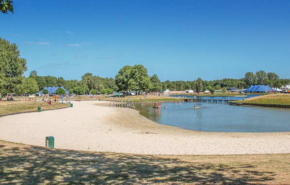 A sandy beach area with a calm lake, surrounded by trees and tents.