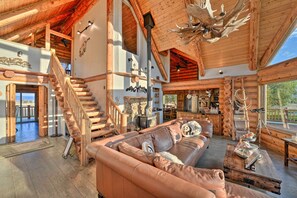 A spacious log cabin interior with a wooden staircase, a large leather sofa, and a dining area.