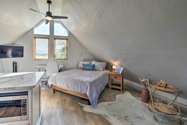 A bedroom with a bed, a desk, a TV, and a ceiling fan.