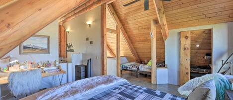 A cozy attic bedroom with a sloped ceiling, a bed with a plaid bedspread, a desk with a lamp, and a ceiling fan.