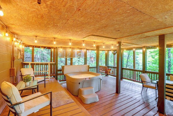 Een houten terras met een jacuzzi, zitplaatsen en sfeerverlichting.