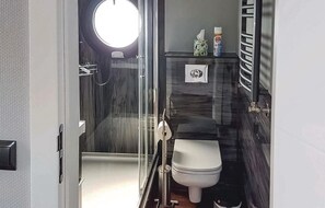 Et lille badeværelse med brusekabine i glas, toilet og en lille vaskebordsektion.