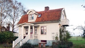 A two-story house with a red-tiled roof, a porch with steps, and a small table outside. - Amazing Home in Degerhamn With 2 Bedrooms and Wifi (Degerhamn)