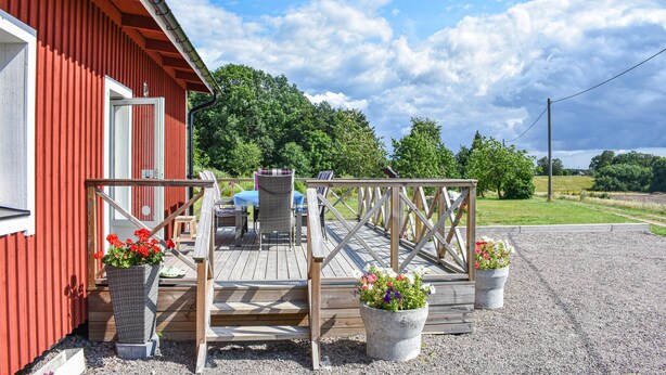 A red building with a wooden deck, outdoor seating, and potted plants.
