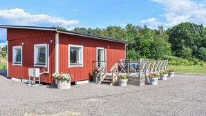 A red building with a gravel driveway and a wooden deck with chairs and potted plants.