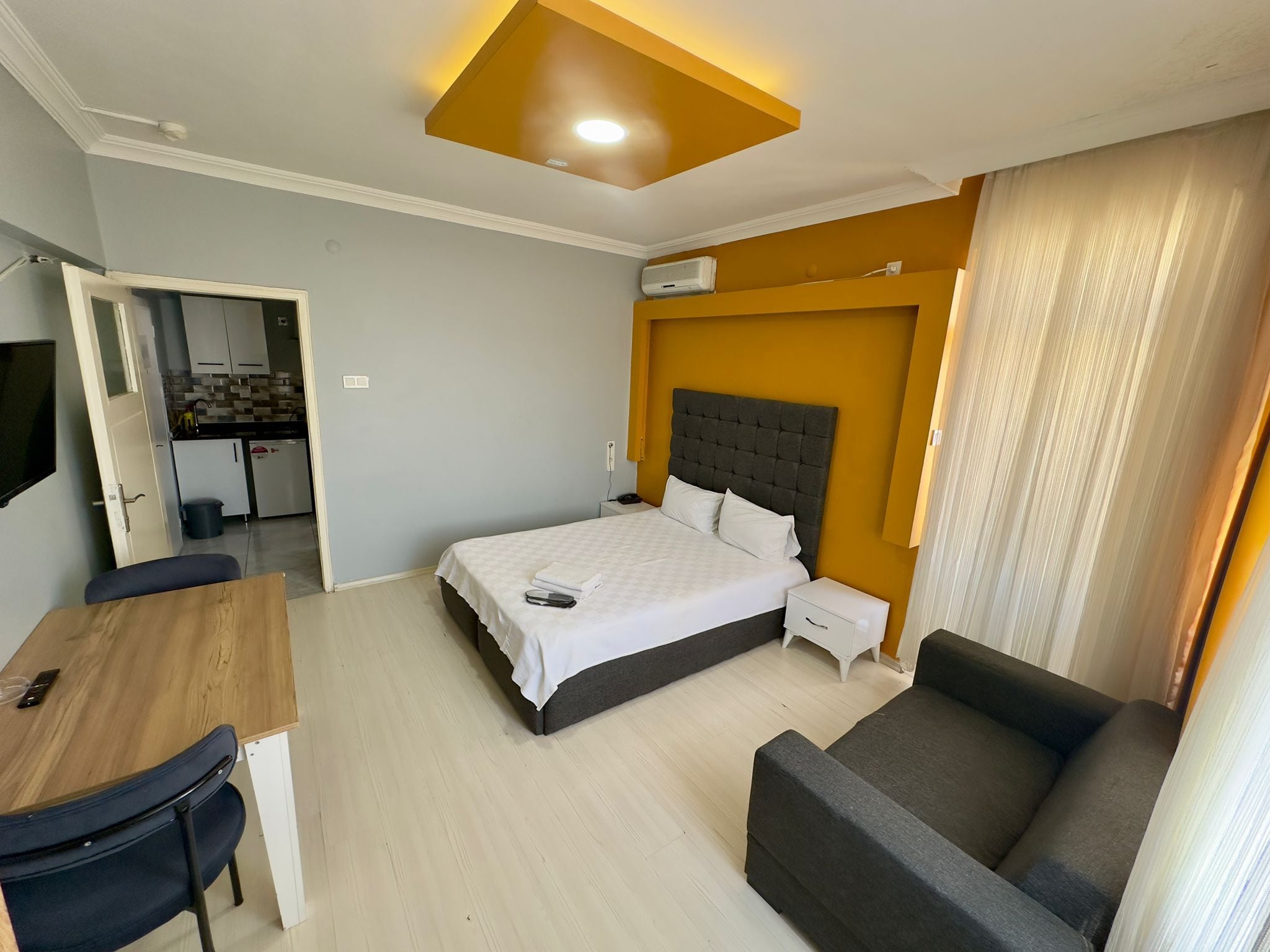 Quarto de hotel com cama, escrivaninha, poltrona, sofá, cozinha compacta e banheiro.