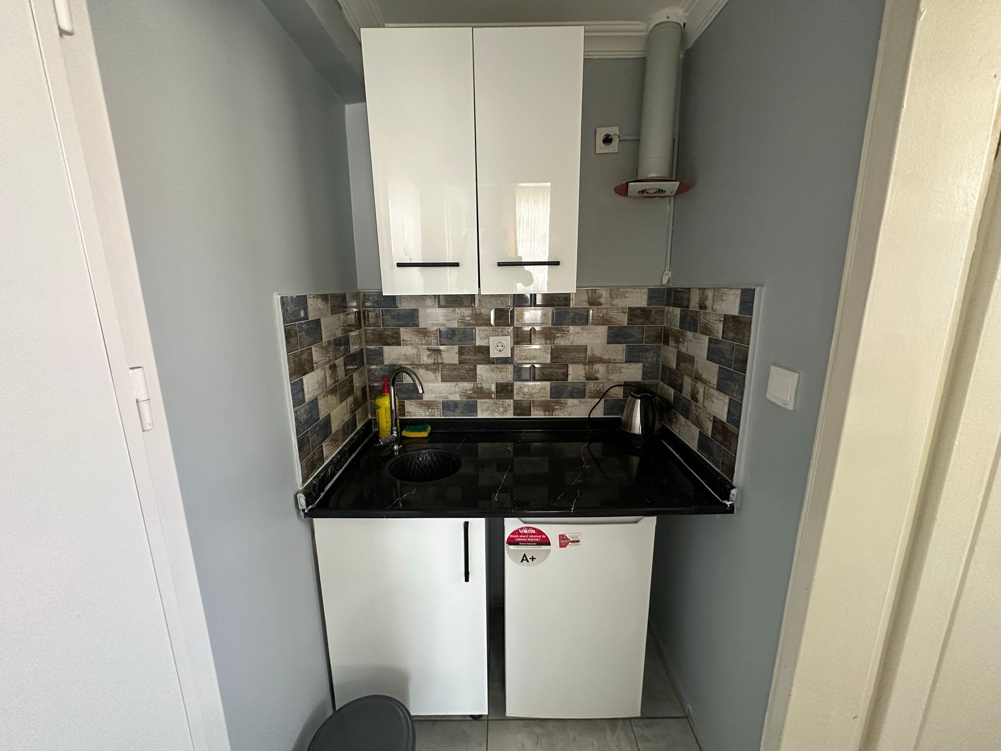 A compact kitchen with white cabinets, a tiled backsplash, and a black countertop.