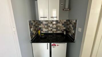 A compact kitchen with white cabinets, a tiled backsplash, and a black countertop.
