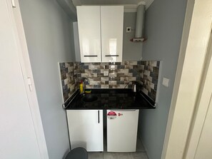 A compact kitchen with white cabinets, a tiled backsplash, and a black countertop. - YILDIRIM SUİT APART OTEL (Ankara)