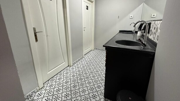 Un pasillo estrecho con baldosas de diseño, dos puertas blancas y un baño pequeño con un lavabo y espejo negros.