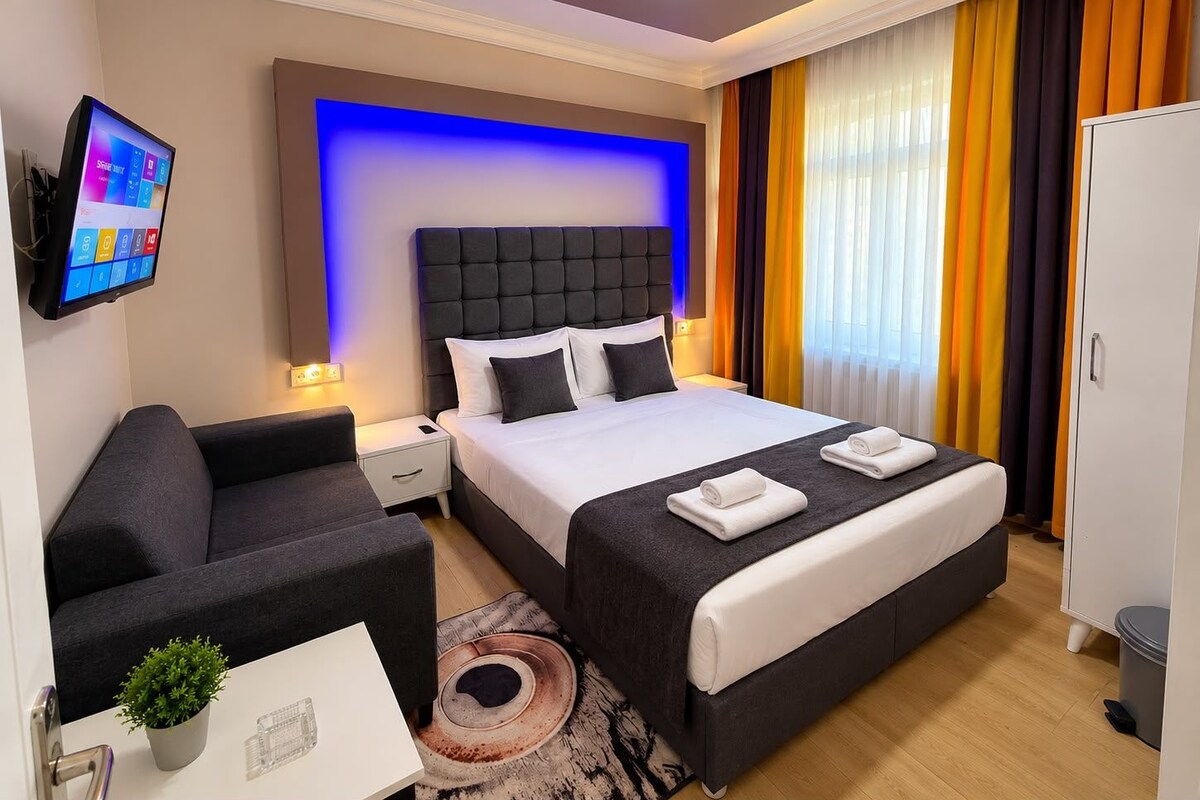 A modern hotel room with a large bed, a desk, a chair, and a television.