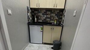 A compact kitchen with a refrigerator, a sink, and a trash bin. - YILDIRIM SUİT APART OTEL (Ankara)