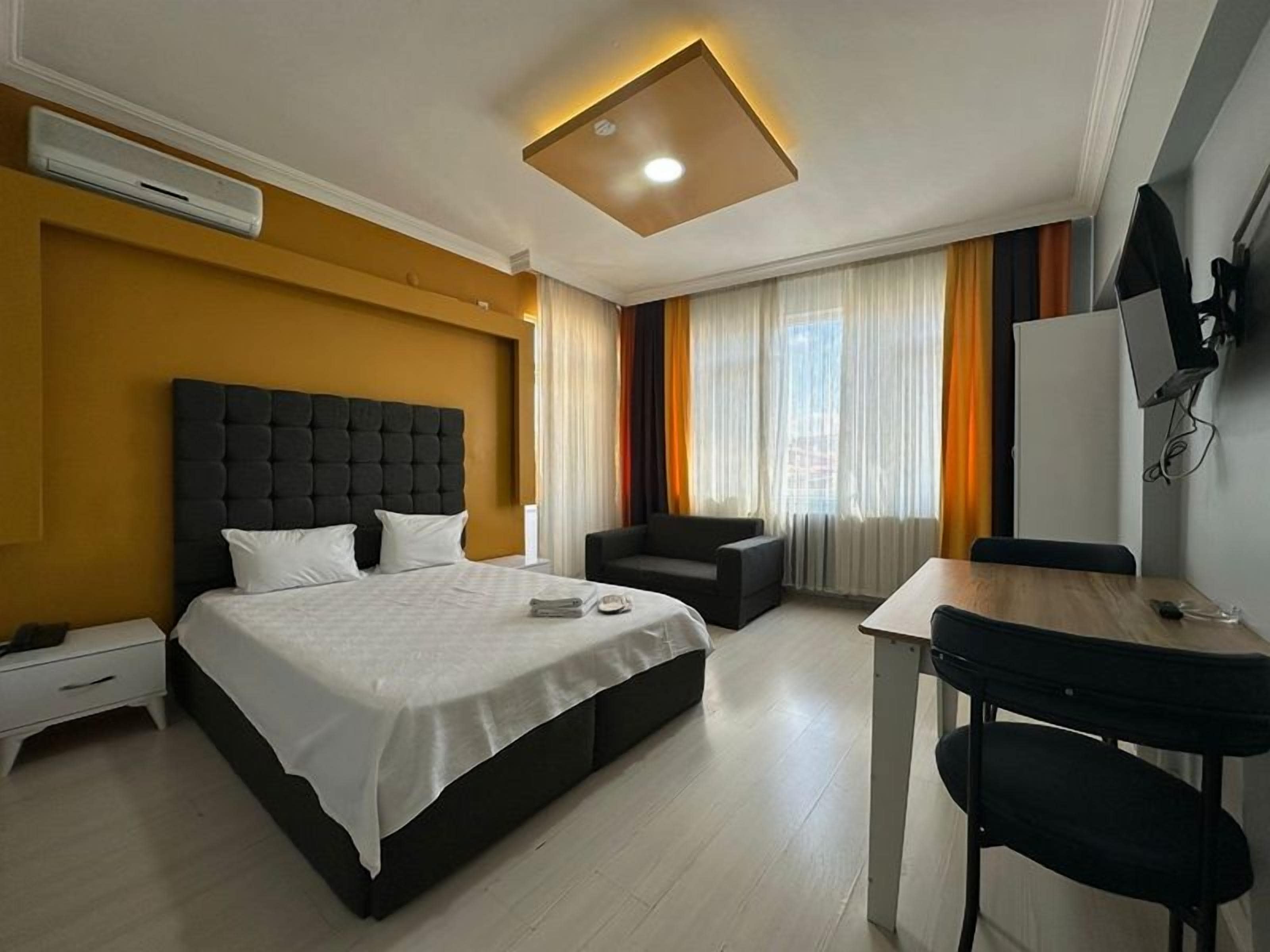 Quarto de hotel com cama, escrivaninha, cadeira e televisão.