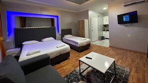 A modern hotel room with two beds, a sofa, a TV, and a small kitchen area. - YILDIRIM SUİT APART OTEL (Ankara)