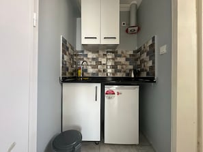 Una cocina compacta con armarios blancos, salpicadero de azulejos y un refrigerador pequeño.