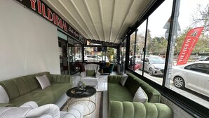 A modern interior with green sofas, a small coffee table, and a large window offering a view of parked cars outside. - YILDIRIM SUİT APART OTEL (Ankara)