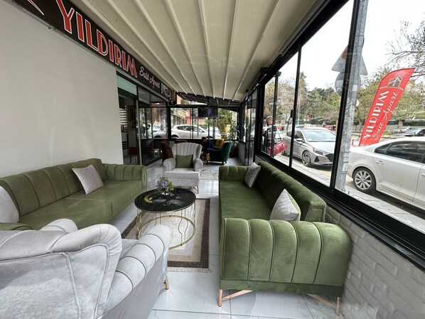 A modern interior with green sofas, a small coffee table, and a large window offering a view of parked cars outside. - YILDIRIM SUİT APART OTEL (Ankara)