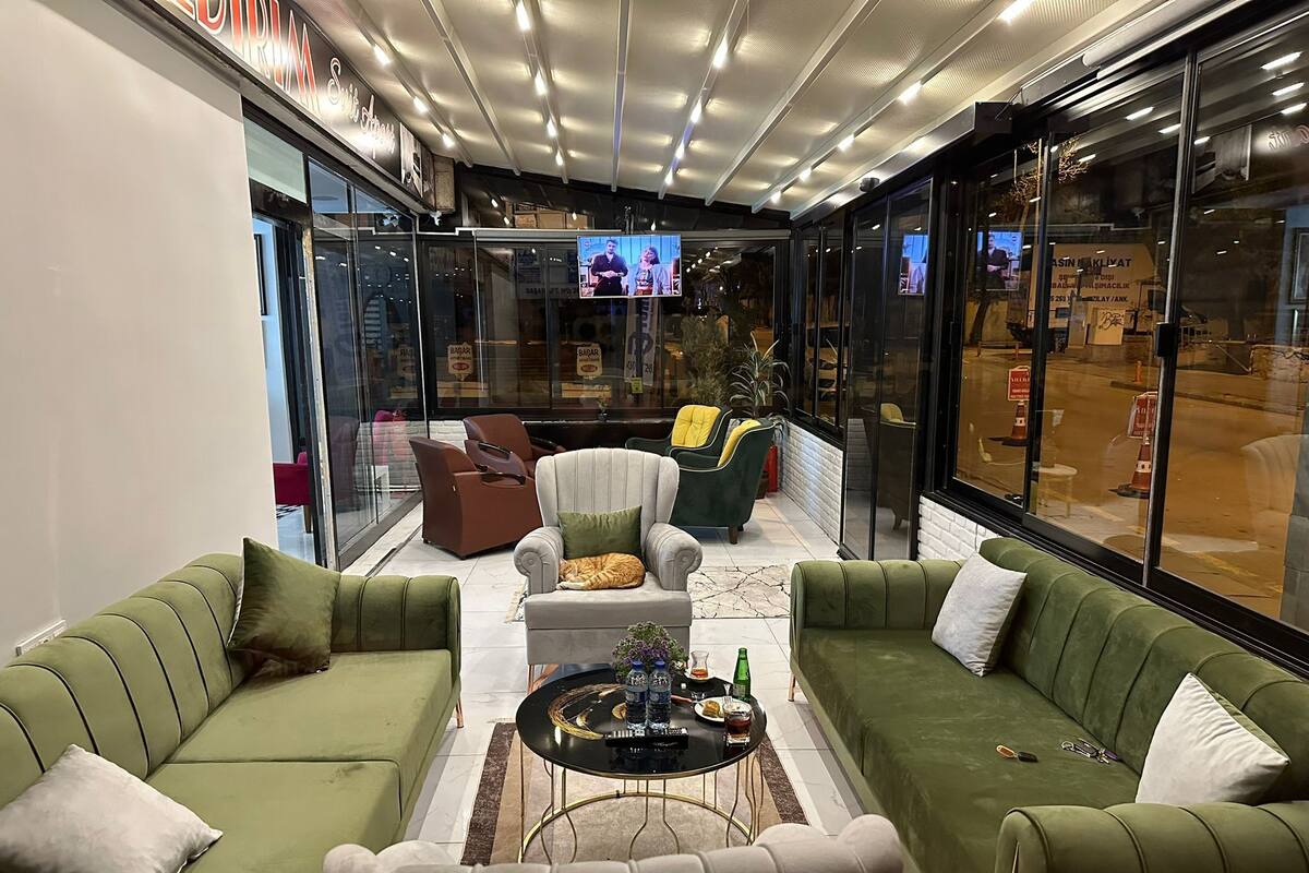 A modern lounge area with green sofas, a round coffee table, and a television screen displaying a program.