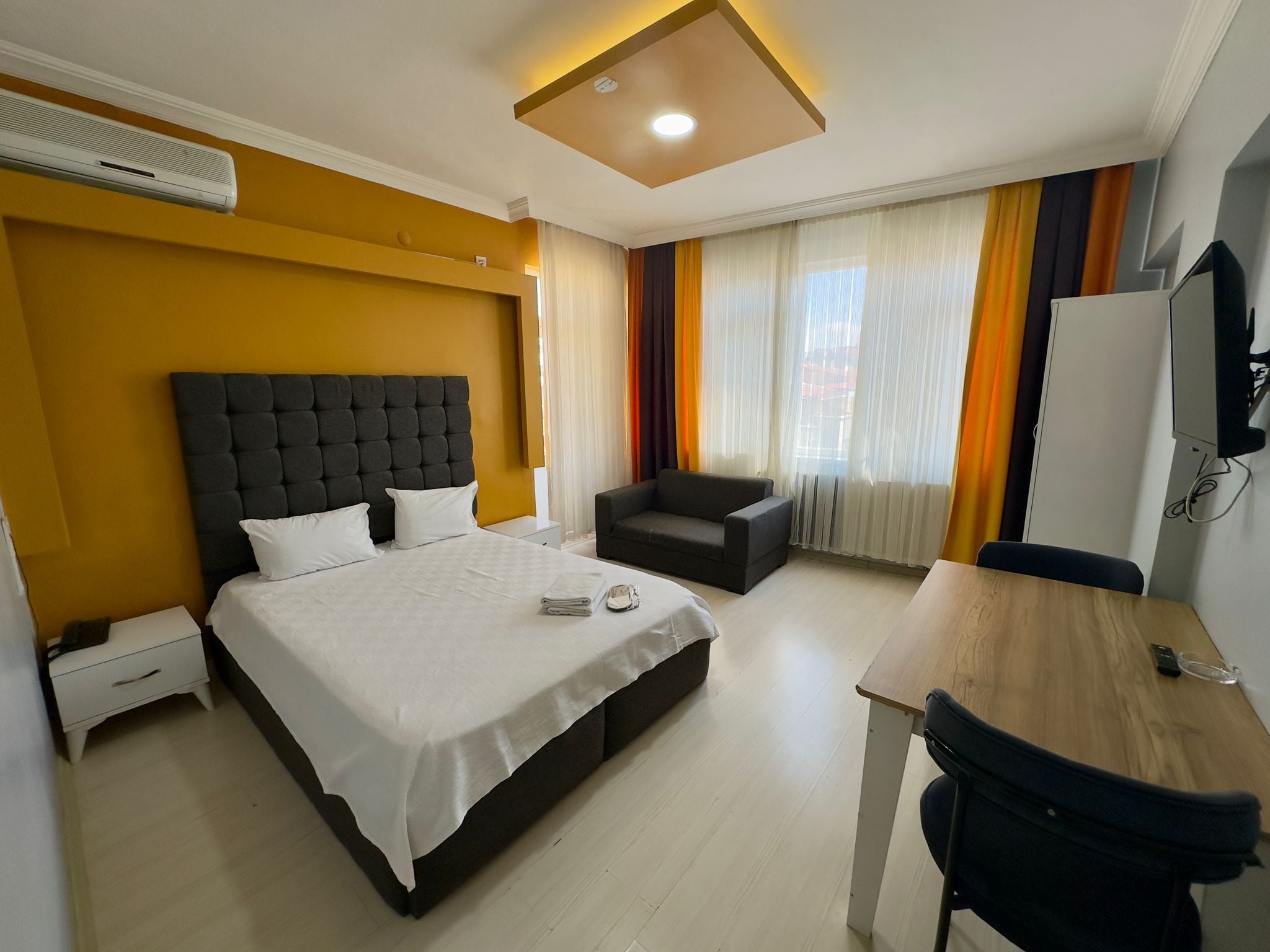 Una habitación de hotel con cama, escritorio, silla, televisor y ventana con cortinas.
