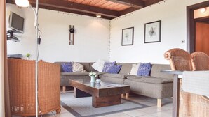 Una sala de estar acogedora con un sofá gris, una mesa de centro de madera, sillas de mimbre y un reloj en la pared.