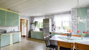 Een keuken met groene kastjes, een roestvrijstalen koelkast en een eettafel met stoelen.