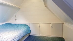 Un dormitorio con techo inclinado, una cama con colcha azul y armarios blancos.