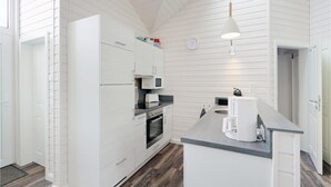 Moderni keittiö, jossa on valkoiset kaapit, sisäänrakennettu uuni, mikroaaltouuni ja kahvinkeitin työtasolla.