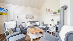 Moderni olohuone, jossa on harmaa sohvaryhmä, puinen sohvapöytä, seinälle asennettu televisio, kirjahylly ja takka.