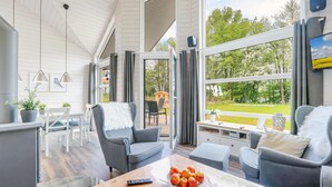 Moderni olohuone, jossa on suuri ikkuna, harmaat sohvat, puinen sohvapöytä, jossa on omenoita, ja kaukosäädin.