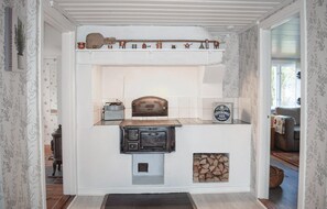 Een landelijke keuken met een houtkachel, een plank met keukengerei en een decoratief metalen bord.