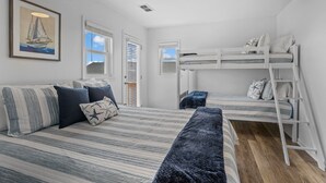 A room with a bunk bed, a sofa with striped cushions, a framed picture of a sailboat, and a window with blinds.
