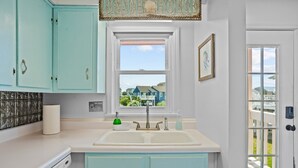 A kitchen with turquoise cabinets, a white countertop, a double sink, and a view of the beach through a window.