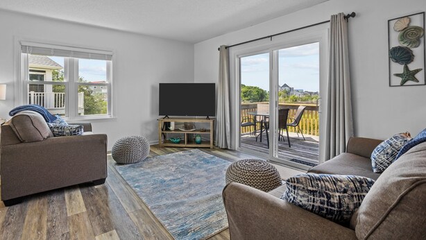 A living room with a flat-screen TV, a sofa, a coffee table, and a large window with curtains.