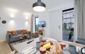 Un salon moderne avec un canapé, une table à manger dressée pour un repas et un téléviseur fixé au mur.