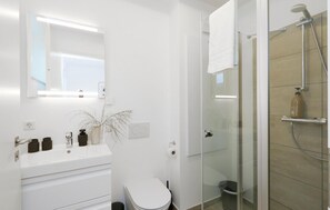 Une salle de bain moderne avec un meuble-lavabo blanc, des toilettes, une douche en verre et un miroir.