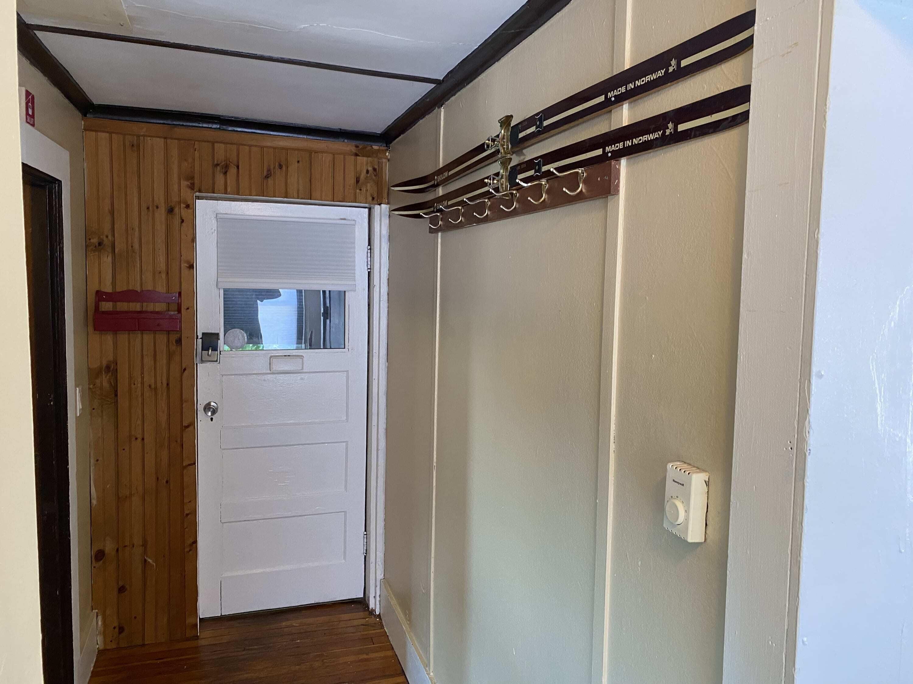Un pasillo estrecho con una puerta de madera y un perchero con letreros que indican 'Hecho en Noruega'.