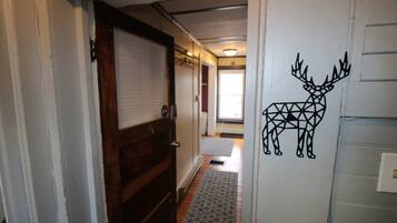 A hallway with a wooden door, a patterned rug, and a wall decal of a geometric deer.
