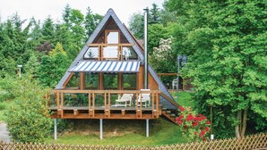 Une cabane en bois avec un toit en pente, une terrasse avec des chaises et un jardin parsemé de fleurs rouges.