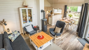 A cozy living room with a sofa, chairs, a table, a cabinet with glass doors, a wood-burning stove, and a view of the kitchen and outdoor area. - Amazing Home in Krems Ii/warderbrück With 2 Bedrooms, Sauna and Wifi (Krems II)