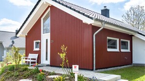 A red single-story house with a white door and windows, a chimney, and a small garden with a bench and flowers. - Amazing Home in Krems Ii/warderbrück With 2 Bedrooms, Sauna and Wifi (Krems II)