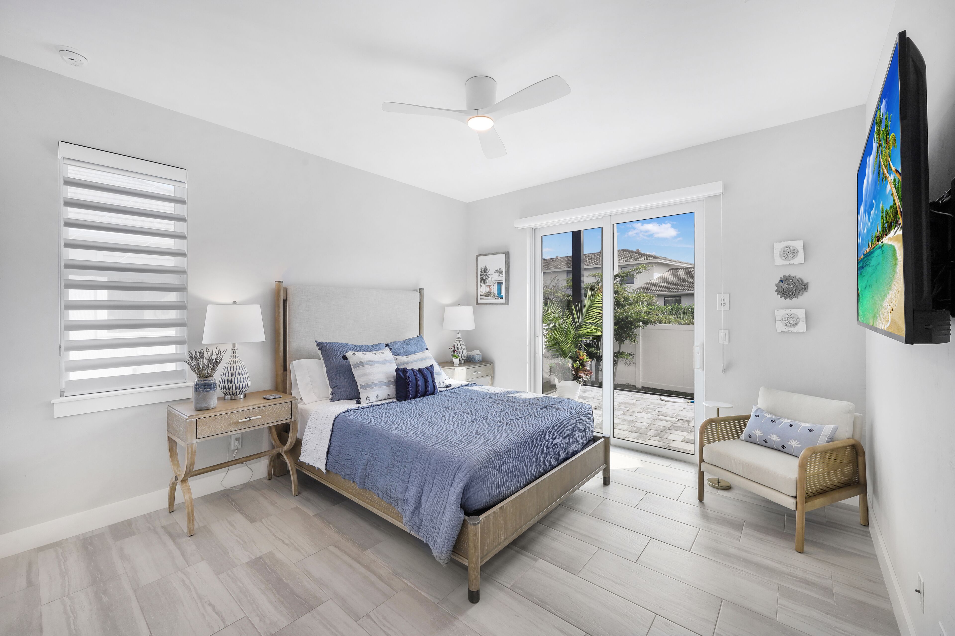 Une chambre à coucher comprenant un lit, des tables de chevet, une chaise, un ventilateur de plafond et une grande fenêtre.