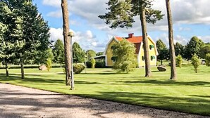 A yellow house with a red roof, surrounded by trees and a well-maintained lawn.