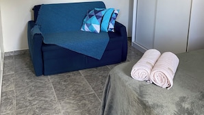 A room with a dark blue sofa, a flat-screen TV on the wall, and a bed with a rolled towel. - Apartamento encantador (Florianópolis)