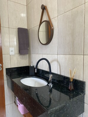 A bathroom with a black marble sink, a round mirror, and a towel rack. - Apartamento encantador (Florianópolis)