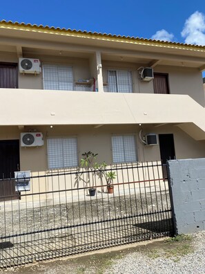 A two-story building with multiple air conditioning units, a gated entrance, and potted plants. - Apartamento encantador (Florianópolis)