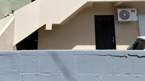 A building with a beige exterior, a dark door, and two air conditioning units mounted on the wall. - Apartamento encantador (Florianópolis)