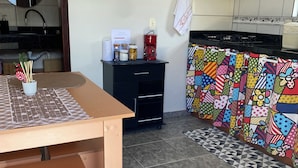 A kitchen with a dining table, a black cabinet, colorful kitchen towels, and a tiled floor. - Apartamento encantador (Florianópolis)