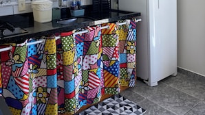 A kitchen with a refrigerator, microwave, and a window with blinds. - Apartamento encantador (Florianópolis)